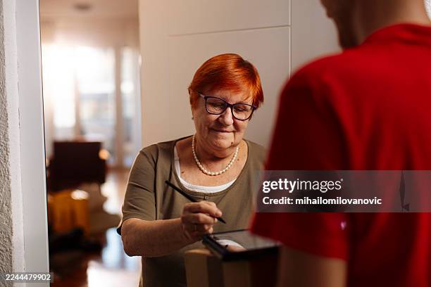 amable anciana con gafas con repartidor en la puerta de casa - entrega sin contacto fotografías e imágenes de stock