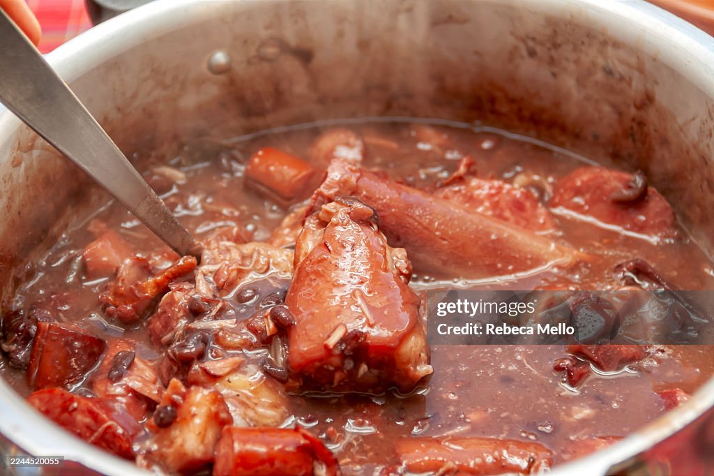Viewed from above, homemade Brazilian feijoada in a pot with a ladle in the center showing pieces of pork tail that may be part of this traditional Brazilian stew.
