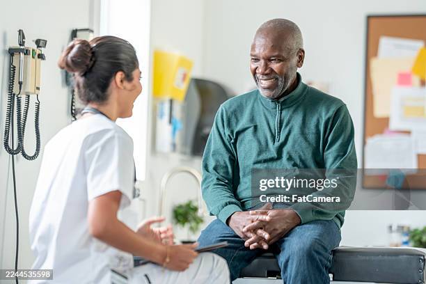 smiling black male patient talks with friendly female nurse in clinic consultation during medical visit today - patience stock pictures, royalty-free photos & images