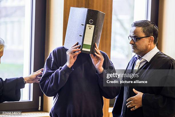 November 2025, North Rhine-Westphalia, Aachen: The accused nurse stands with a file folder in front of his face next to his lawyer Volker Breyer in...