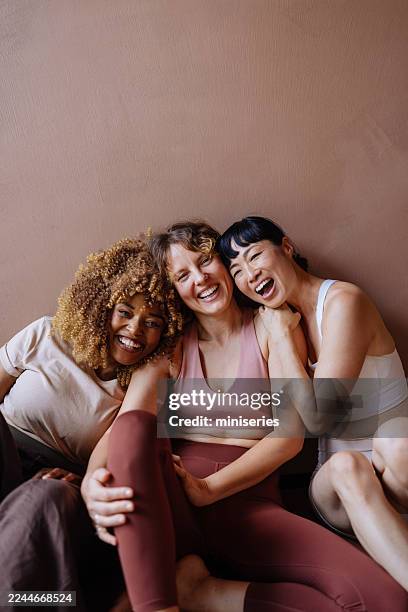 three friends laughing together during casual workout session, sitting against pink wall - group of objects stock pictures, royalty-free photos & images