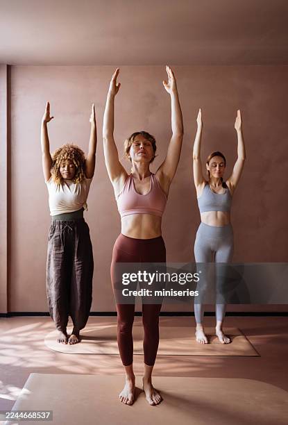 three women practicing yoga in a calm indoor studio during a gentle group class session - mountain pose stock pictures, royalty-free photos & images