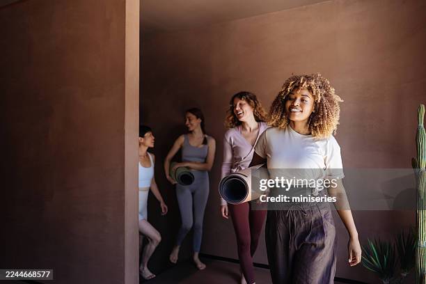 friends in yoga gear walk with mats through warm studio corridor before class - yoga class stock pictures, royalty-free photos & images