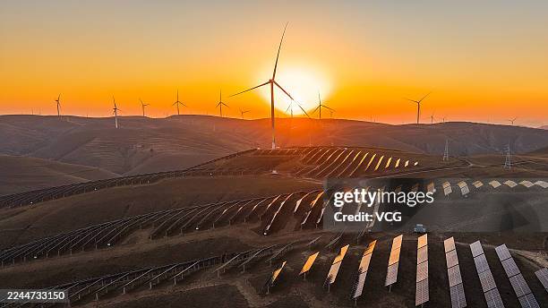 In an aerial view, sunset glow lights up wind turbines and rows of solar panels at a wind farm on October 28, 2025 in Qingyang, Gansu Province of...
