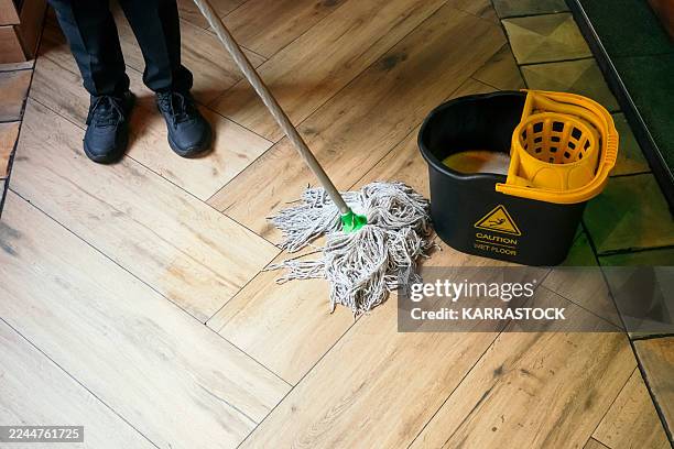 person mopping wooden floor next to caution bucket. - mop stock pictures, royalty-free photos & images