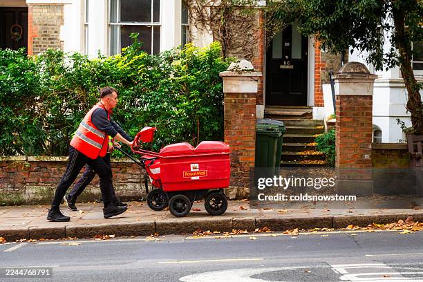 royal mail postman pushing mail trolley on london city street - postal worker stock pictures, royalty-free photos & images