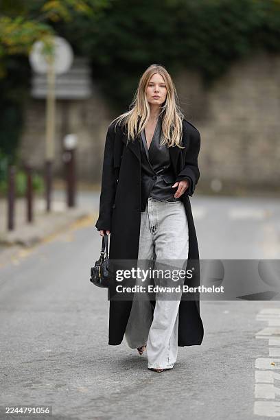 Natalia Verza wears long straight blonde hair, a black wool long coat by The Frankie Shop, a black leather double-breasted jacket by L’Agence, light...