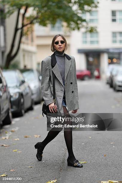 Emy Venturini wears light brown hair tied in a low ponytail, round metal sunglasses by Ray-Ban, a grey wool vintage blazer jacket by YSL layered over...