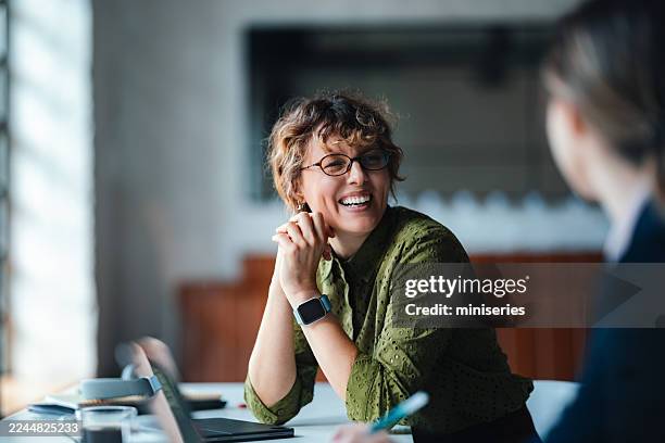 smiling woman in green shirt engages in casual business meeting at modern coworking space - business meeting stockfoto's en -beelden