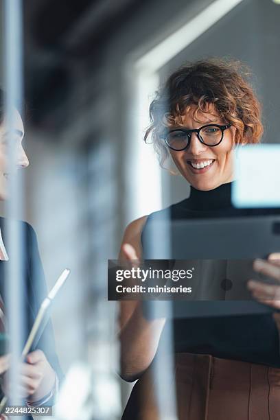 smiling woman with glasses holding tablet at coworking space during business meeting - venture capital stock pictures, royalty-free photos & images