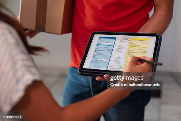 delivery person uses tablet to fill digital form while customer holds package - entrega sem contacto imagens e fotografias de stock