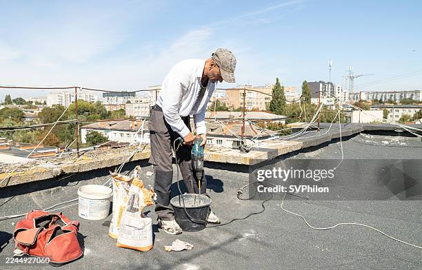 der bauarbeiter bereitet auf dem dach eine klebstoffmischung für die isolierung der gebäudefassade mit styroporplatten vor. - elektrisches werkzeug stock-fotos und bilder