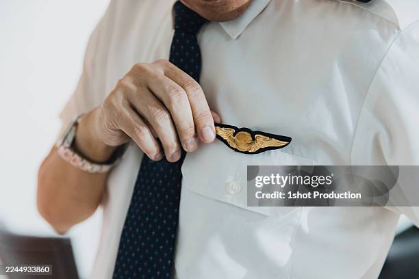 pilot adjusts uniform insignia while preparing for flight in a modern airline office - pilot uniform stock pictures, royalty-free photos & images