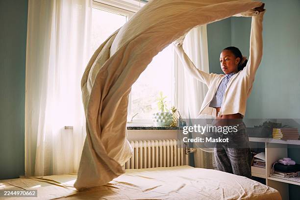 girl spreading sheet on bed in bedroom at home - chambre bien rangée photos et images de collection