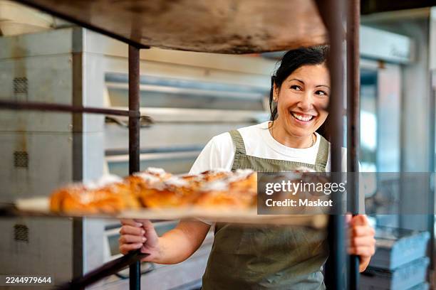 happy female baker pushing trolley loaded with cinnamon buns - foodservice stockfoto's en -beelden