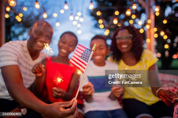 joyful black family celebrates outdoors with sparklers and american flag during evening celebration - real family stock pictures, royalty-free photos & images