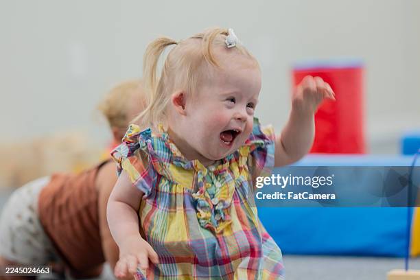 joyful blonde toddler laughs in colorful plaid dress at daycare center during playtime - babymeisjes stockfoto's en -beelden