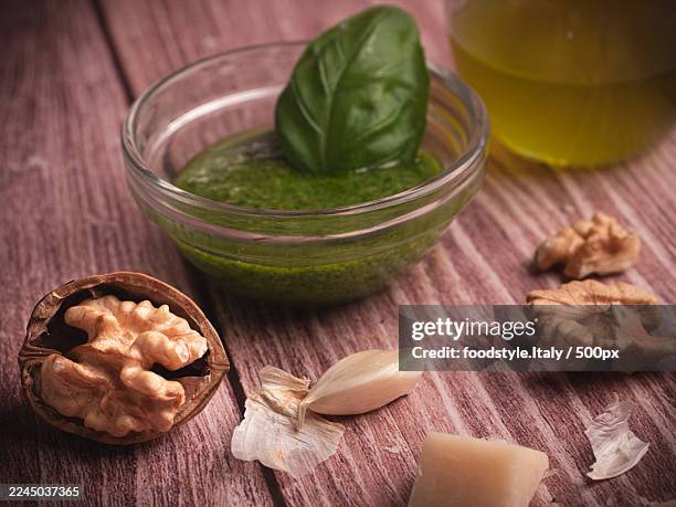 high angle view of ingredients for pesto sauce on a wooden table, including basil, walnuts, garlic, and olive oil - pistou photos et images de collection