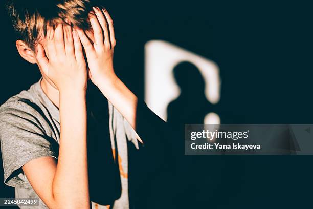 frightened or tired boy covers face in a moment of distress - abuso di minore foto e immagini stock