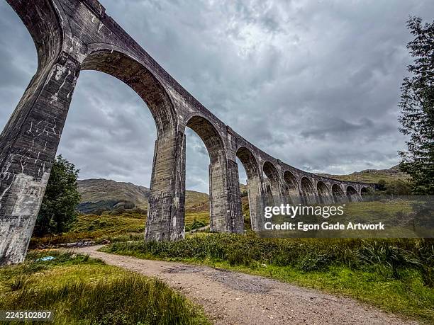 majestic stone viaduct arches stretch across lush green landscape under an overcast sky. glenfinnan viaduct, scotland - viaduct stock pictures, royalty-free photos & images