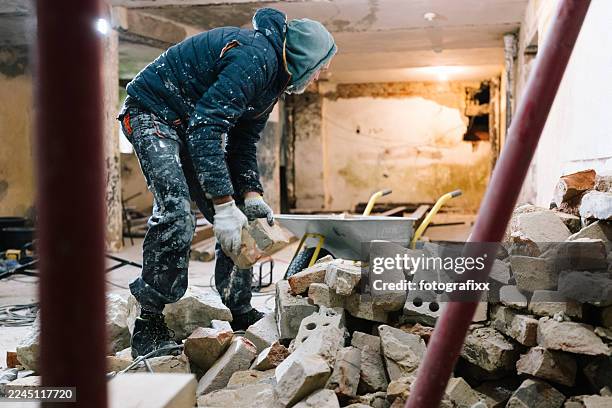 un ouvrier du bâtiment jette des briques dans une brouette - retraités qui travaillent photos et images de collection