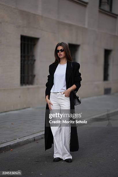 Iva Nikolina is seen wearing a long black wool coat with structured shoulders and a straight silhouette by Almada Label; a white fitted cotton...