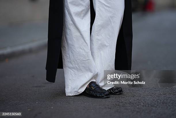 Iva Nikolina is seen wearing a long black wool coat with structured shoulders and a straight silhouette by Almada Label; white wide-leg jeans in a...