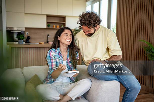 young couple laughing planning future sitting on sofa - girlfriend stock pictures, royalty-free photos & images