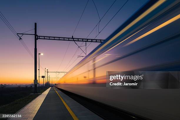 light trail of fast train passing through railway station in landscape at golden dawn - carruagem imagens e fotografias de stock