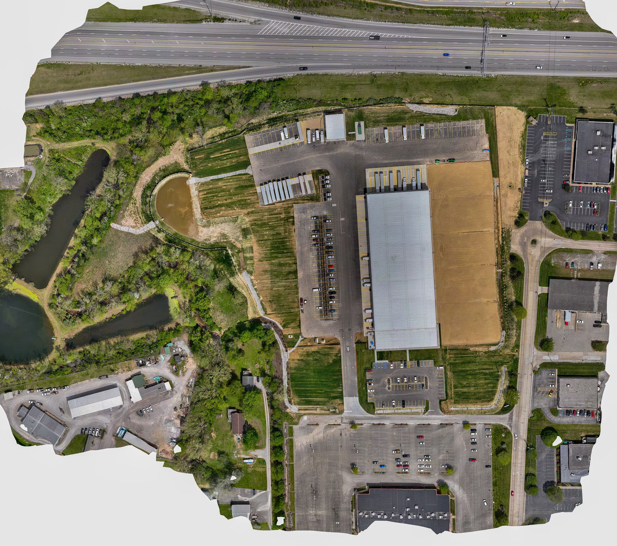High-resolution drone orthomosaic aerial map of an industrial facility featuring a large warehouse, parking lots, retention pond, and adjacent highway High-resolution drone orthomosaic aerial map of an industrial facility featuring a large warehouse, parking lots, retention pond, and adjacent highway
