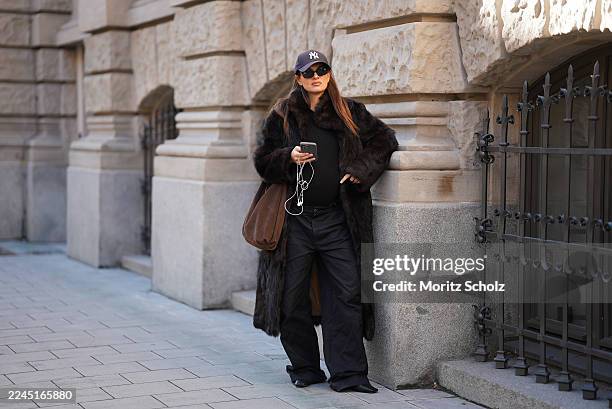 Anna Winter is seen wearing a long dark brown calfskin and fur coat with a wide collar and relaxed fit by Gant; a fitted black top by Comma; black...
