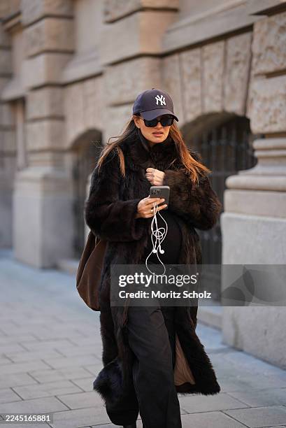 Anna Winter is seen wearing a long dark brown calfskin and fur coat with a wide collar and relaxed fit by Gant; a fitted black top by Comma; black...