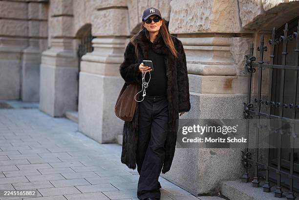Anna Winter is seen wearing a long dark brown calfskin and fur coat with a wide collar and relaxed fit by Gant; a fitted black top by Comma; black...