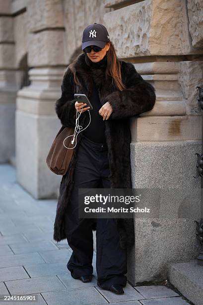 Anna Winter is seen wearing a long dark brown calfskin and fur coat with a wide collar and relaxed fit by Gant; a fitted black top by Comma; black...