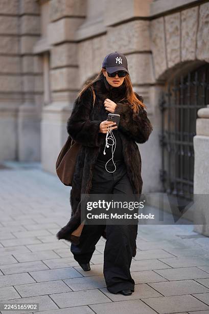 Anna Winter is seen wearing a long dark brown calfskin and fur coat with a wide collar and relaxed fit by Gant; a fitted black top by Comma; black...