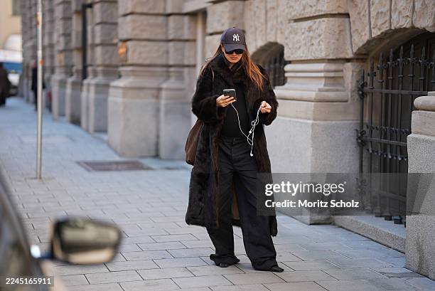 Anna Winter is seen wearing a long dark brown calfskin and fur coat with a wide collar and relaxed fit by Gant; a fitted black top by Comma; black...