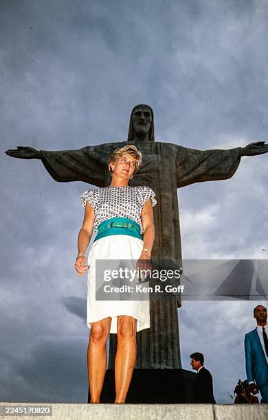 Diana, Princess of Wales, wearing a patterned short-sleeve top with a white mid-length skirt and green waistband, stands in front of the Christ the...