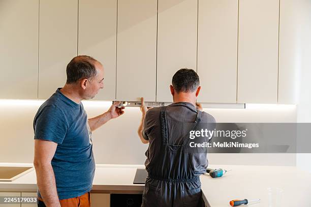 two workers installing modern kitchen hood with tools on counter - appliance installation stock pictures, royalty-free photos & images