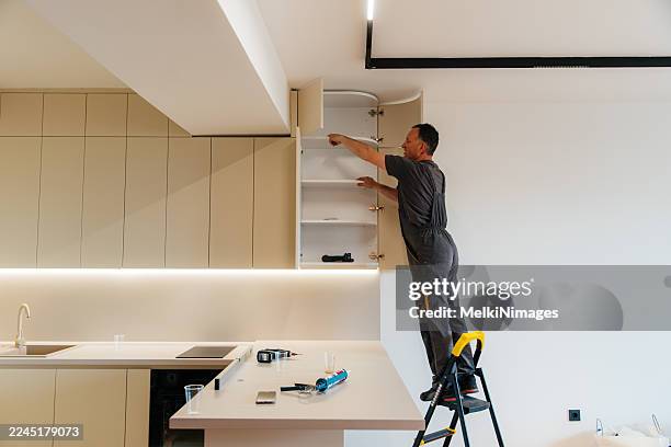 worker installing upper kitchen cabinets on ladder - tool cabinet stock pictures, royalty-free photos & images