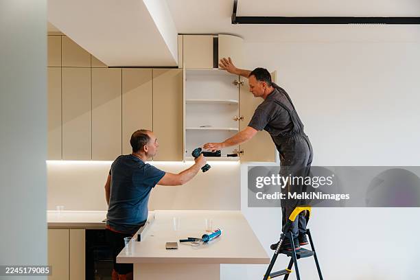two workers installing upper kitchen cabinets together - carpentry stock pictures, royalty-free photos & images