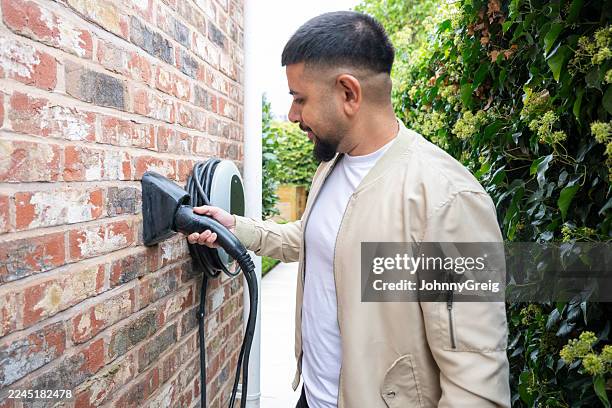british asian man removing electric car charging cable from wall - mid adult stock pictures, royalty-free photos & images