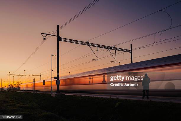 man waiting on platform with passing train in motion blur at dawn - stimmungsvoller himmel stock-fotos und bilder