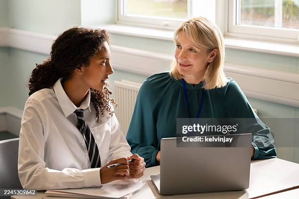lehrer, der laptop benutzt, spricht mit gymnasiastin im klassenzimmer - studiengebühren stock-fotos und bilder