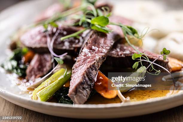 the plate is arranged with slices of beef, sirloin or flank steak. the meat is cooked to medium rare, with a distinct pink to red center and a dark, more browned crust. the slices are stacked on vegetables and the dish is served with mashed potatoes. - blue cheese dressing stock pictures, royalty-free photos & images