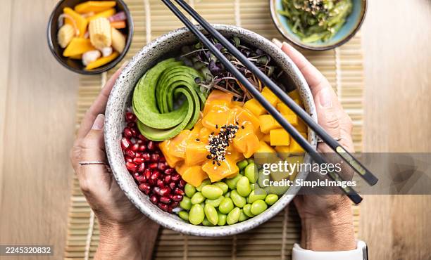 a top view of a poke bowl held in both hands by a person sitting at a table. - mangue photos et images de collection