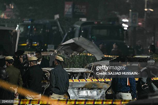 Police and security personnel stand behind the safety cordons delimiting the blast site as they inspect charred vehicles following an explosion near...