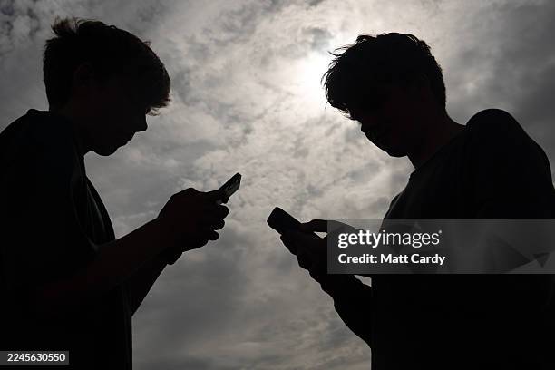 Two teenagers look at their iPhone smart phone screens on August 26, 2025 in Penzance, England. The amount of time children spend on screens each day...