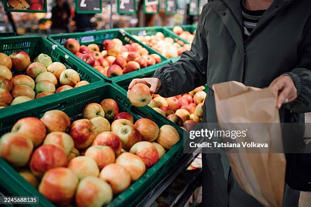 customer selects fresh apples from green crates at a bustling grocery market - greengrocer stock pictures, royalty-free photos & images