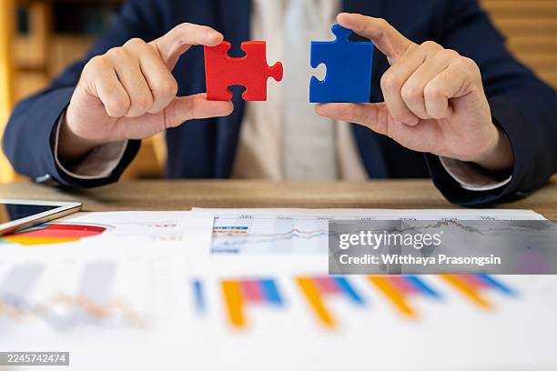 businessperson connecting puzzle pieces over financial charts - fusionen und übernahmen stock-fotos und bilder