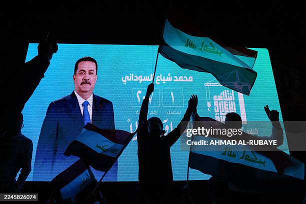 Supporters of incumbent Iraqi Prime Minister Mohammed Shia al-Sudani wave national flags in front of a screen displaying his portrait as they...